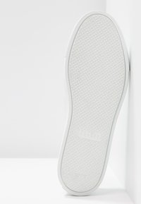 Semelle d'une basket blanche avec motif de grip texturé, nom de la marque et inscription « Made in Italy » sur une surface blanche.