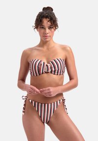 Set bikini a righe in rosso, blu navy e crema. Top bandeau con dettaglio a fiocco; parte inferiore con lacci laterali e dettagli di pom-pom. Tessuto dalla texture liscia.