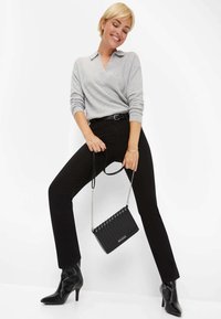 Pull gris en V avec des manches retroussées, jean noir ajusté, bottes à talons aiguilles noires, et un sac bandoulière noir texturé avec une chaîne.