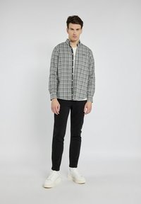 Szara koszula w kratę zapinana na guziki z kołnierzykiem, noszona na białej koszulce. Czarne spodnie i białe trampki dopełniają outfit. Prosty design i dopasowanie.