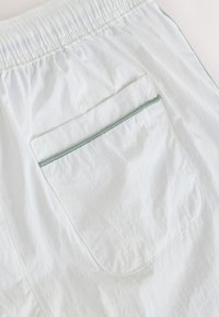 Hvide shorts i letvægtigt stof med elastisk taljebånd og en enkelt baglomme med grøn kant og lynlås.