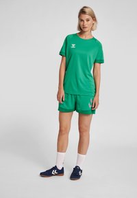 Grøn atletisk skjorte med matchende shorts, lavet af åndbart stof. Har et logo på skjorten og kontrasterende detaljer på shortsene.