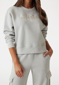 Lichtgrijs sweatshirt met geborduurd "GUESS EST. 1981" logo, geribbelde manchetten en een relaxed fit, gecombineerd met bijpassende broek.