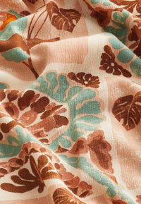 Tissu léger avec un motif floral dans des teintes de marron, de bleu-vert et de rose doux. La texture est légèrement froissée et douce au toucher.
