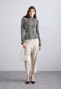 Maglione a collo alto a righe bianche e nere, con silhouette aderente. Pantaloni beige chiaro a gamba affusolata e una piccola borsa color crema. Décolleté neri a punta.