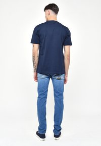 Marinblå bomullströja med korta ärmar, kombinerad med ljusblå denimjeans. Jeansen har en dekorerad design på bakfickan.
