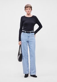 Μαύρη μπλούζα με μακριά μανίκια, ανοιχτό μπλε φαρδιά τζιν, μαύρη ζώνη και μικρή μαύρη τσάντα χειρός; λεία υφάσματα με άνετη εφαρμογή.