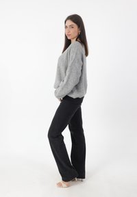 Maglione lavorato a maglia grigio con spalle scese abbinato a jeans neri a vita alta svasati e tacchi beige. Outfit semplice e casual.