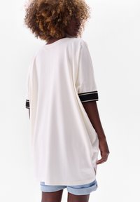 White oversized t-shirt with short sleeves, featuring black striped accents on cuffs. Soft fabric with a relaxed fit, side hem slits.