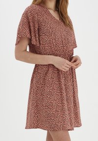 Šaty s krátkým rukávem a véčkovým výstřihem v barvě rzi s puntíkovaným vzorem v bílé a černé. Elastický pas a splývavý materiál.