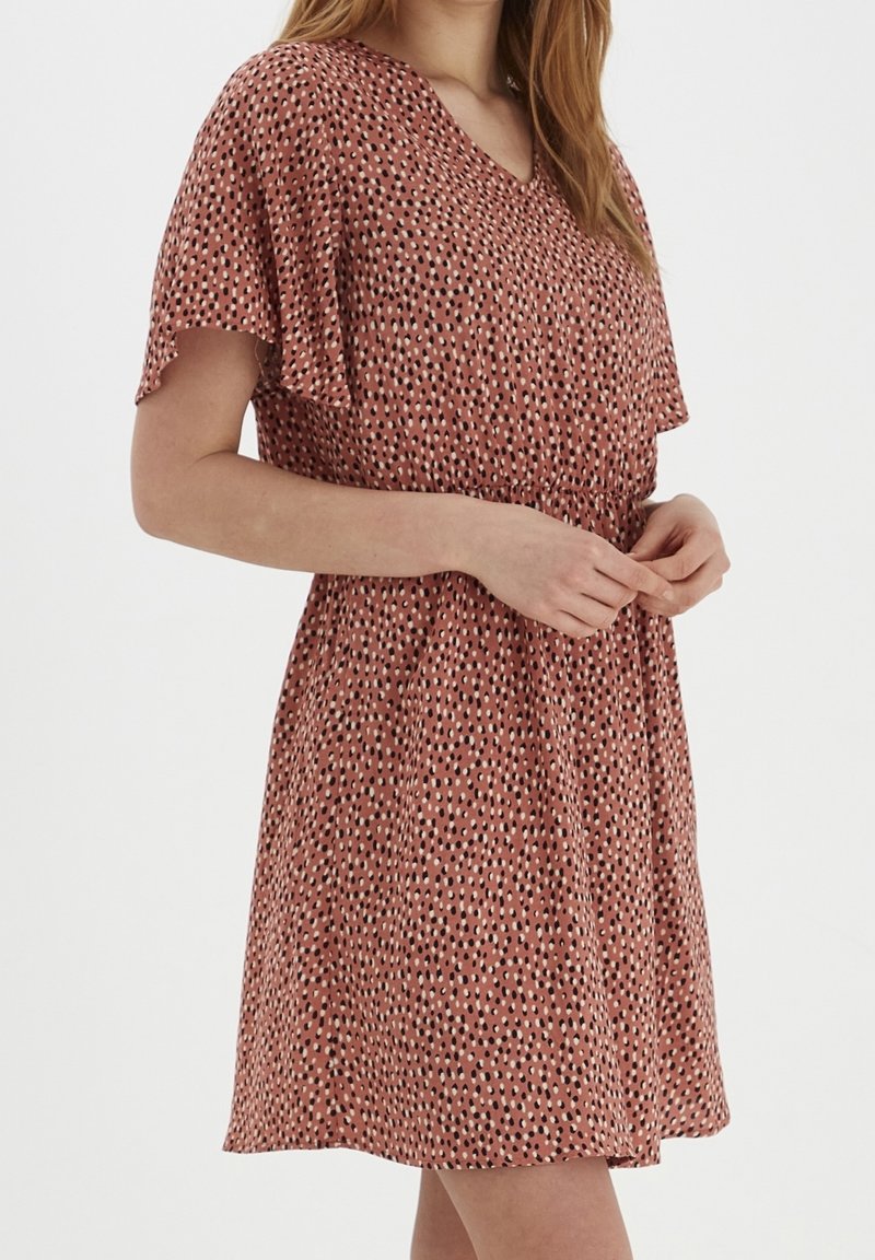 Šaty s krátkým rukávem a véčkovým výstřihem v barvě rzi s puntíkovaným vzorem v bílé a černé. Elastický pas a splývavý materiál.