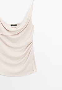 Mouwloze top met cowl-hals in lichtbeige stof, met zachte draping van de halslijn naar beneden, een soepele textuur en een onderrand die gebogen is.