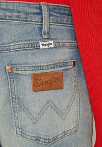 Wrangler plave traperice imaju kožnu oznaku s logom, bakrene zakovice i karakterističnu cik-cak šav na stražnjem džepu.