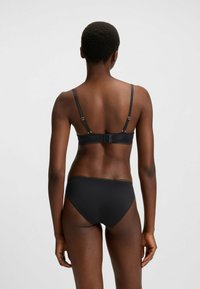 Conjunto de lingerie preta com um sutiã sem emendas, com alças ajustáveis e fecho atrás, combinado com uma tanga de cintura baixa. Textura suave.