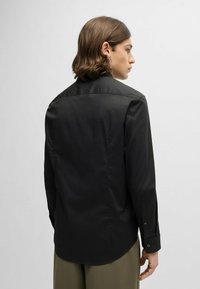 Zwarte shirt met lange mouwen en een kraag, gladde textuur en knoopmanchetten. Heeft een gebogen zoom en een eenvoudig ontwerp.