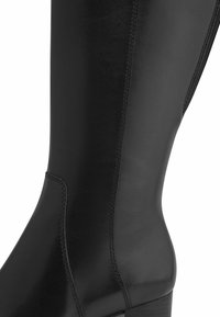 Knee-high black leather boot with a smooth texture, tapered shape, subtle stitching detail, and a stacked heel.