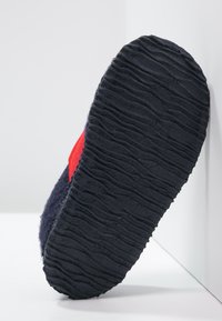 Navyblaue Hausschuhe mit einer strukturierten Gummisohle, die mit einem auffälligen roten Akzent versehen sind. Das Obermaterial ist weich und flauschig und bietet hohen Komfort.