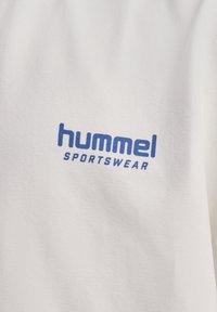 Biała bawełniana koszulka z niebieskim logo "hummel" oraz napisem "SPORTSWEAR". Teksturowana tkanina, okrągły dekolt oraz krótkie rękawy.