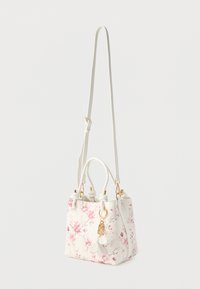 Pequeño bolso blanco con estampado floral rosa, dos asas cortas, una correa larga ajustable y un llavero dorado con pétalos blancos.