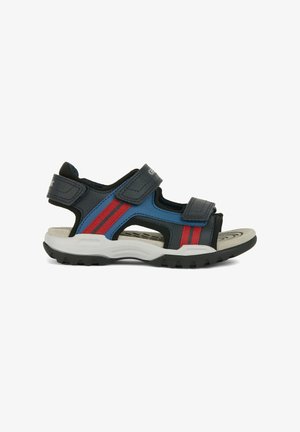 Sandales bleues et noires avec des rayures rouges, fabriquées en matériau synthétique. Elles possèdent deux sangles en Velcro ajustables et une semelle en caoutchouc texturée.