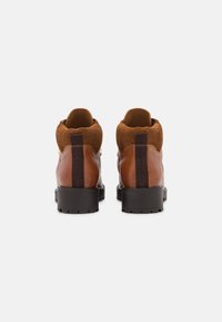 Bottines en cuir marron avec des accents en daim, semelles en caoutchouc noir plat et une languette à l'arrière pour un enfilage facile. Doublure intérieure douce.