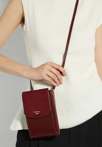 Maroon leather crossbody bag with a flap closure, zippered compartment, and gold branding. It features a slim design and a long strap.