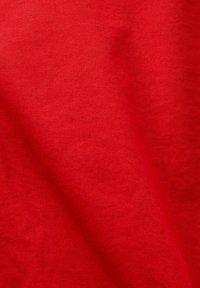 Tissu rouge avec une texture de tissage en diagonale visible et des ombres subtiles mettant en valeur les plis.