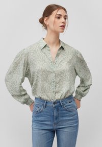 Light green button-up shirt with a floral pattern, long puff sleeves, and elastic cuffs, paired with blue denim jeans.
