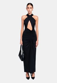 Abito da sera nero con scollo all'americana, dettaglio cut-out frontale, ruches e silhouette aderente. Indossato con tacchi neri e una piccola borsa.