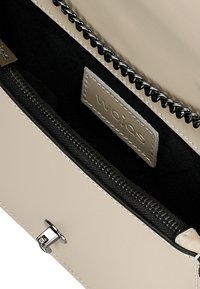 Beige leren handtas interieur met zwarte voering, zilveren rits en een label. Voorzien van een gepolijste sluiting en een gestructureerde afwerking.