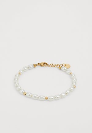 Fehér gyöngy karkötő arany díszítéssel és záróval. Váltakozó sima gyöngyök és kis arany gyöngyök. Hosszabbító láncot tartalmaz az állítható hossz érdekében.