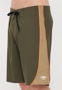 Grüne und beigefarbene Badehose mit orangefarbenen Seitenstreifen, elastischem Bund mit schwarzem Kordelzug und einem weißen Logo auf der unteren rechten Seite.