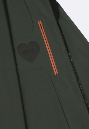 Sezione di giacca verde scuro con una toppa a forma di cuore nera e una tasca con cerniera a strisce verticali arancioni accanto a una cucitura con cerniera nera.