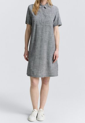 Robe grise à manches courtes avec un col à revers et un motif à carreaux subtil, dotée d'une poche poitrine et d'une coupe décontractée. Portée avec des baskets blanches.