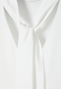 White blouse featuring a soft, lightweight fabric with a tied bow at the neck, displaying a smooth texture and minimalistic design.