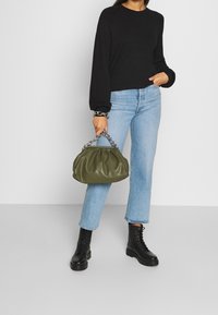 Groene leren handtas met een geplooid ontwerp en een zilveren kettinghandvat, gecombineerd met lichtblauwe jeans en zwarte combat boots. Zwarte trui gedragen.