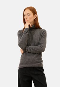 Grauer Rollkragenpullover aus weichem Material, mit lockerem Schnitt und langen Ärmeln. Getragen mit schwarzen, taillierten Hosen.
