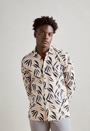 Beige shirt with black leaf pattern, button-up design, long sleeves, and a relaxed fit. Soft fabric with a smooth texture.