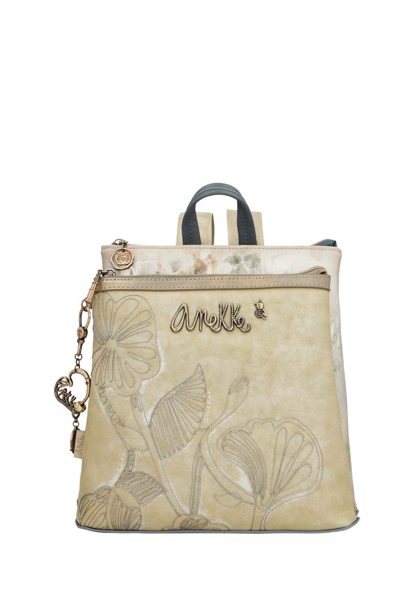 Zaino beige con design floreale in rilievo. Presenta due spallacci, una maniglia superiore e una cerniera metallica con un ciondolo.