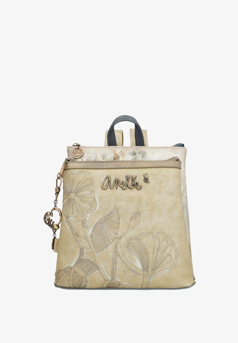 Sac à dos beige avec un design en relief floral. Il dispose de deux bretelles, d'une poignée supérieure et d'une fermeture éclair métallique avec un pendentif.