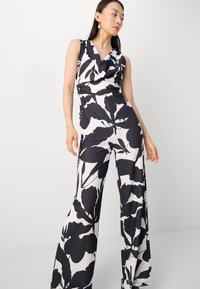 Mono floral en blanco y negro con escote drapeado, piernas anchas y una cintura ajustada. Tejido suave con un acabado brillante.