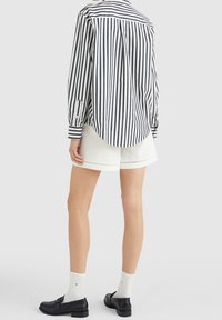 Camisa de botones a rayas blanca y azul marino, de corte relajado, con mangas largas. Combinada con pantalones cortos blancos y mocasines negros, usada con calcetines blancos.