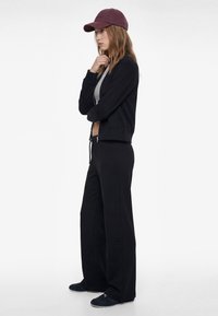 Black cotton zip-up jacket, gray tank top, wide-leg black pants, and dark blue shoes; burgundy cap completes the casual outfit.