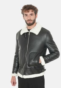 Giubbotto in pelle nera con rifiniture in shearling bianco sul colletto e sui polsini, dotato di una cerniera frontale e due ampie tasche anteriori.