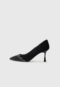 Black suede high-heeled pump with pointed toe, embellished bezel and crystal detailing at the toe cap, featuring a sleek, slender heel.