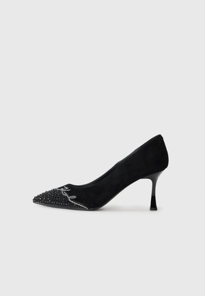 Čierne semišové lodičky na vysokom podpätku so špicatou špičkou, zdobené obrubou a krystalovými detailmi na špičke, s elegantným, štíhlym podpätkom.