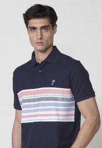 Tamsiai mėlynas polo marškinėliai su dryžuotu dizainu pastelinėmis spalvomis, turintys apykaklę ir tris mygtukus. Subtilus logotipo detalė krūtinėje.