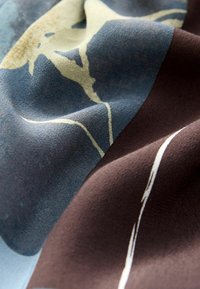 Bunt gemusteter Stoff mit abstrakten Blumenmustern, der in Blau-, Beige- und Brauntönen gehalten ist und eine weiche, strukturierte Oberfläche aufweist.