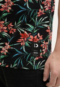 Tkanina w kwiatowy wzór z różowymi i pomarańczowymi kwiatami na czarnym tle; posiada tkany metek na brzegu z nazwą marki i logo.