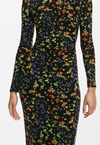 Hosszú ujjú virágmintás ruha fekete bordázott anyagból, narancssárga, lila és zöld virágmintákkal az anyagon.